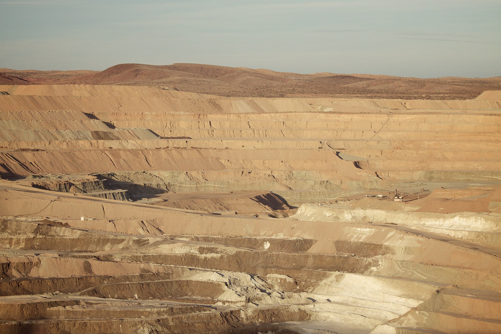 A wide open-pit mine with stepped terraces descending into the earth under a pale desert sky.