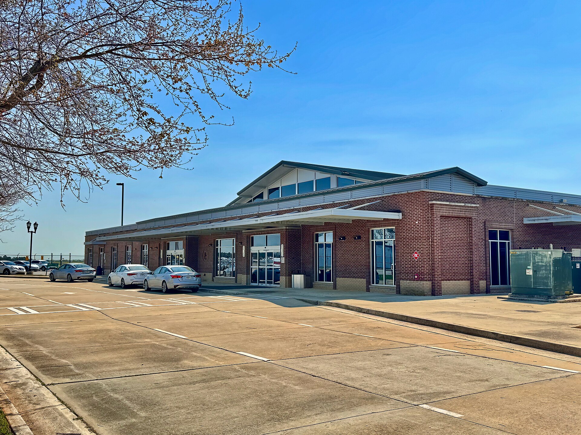 The brick terminal building of a small regional airport with a nearly empty parking lot in front.